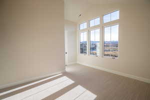 Carpeted empty room featuring high vaulted ceiling and baseboards