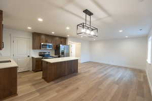 Kitchen featuring a kitchen island, a sink, light countertops, appliances with stainless steel finishes, and light wood-type flooring