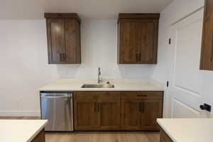 Kitchen featuring dishwasher, light countertops, light wood-type flooring, and a sink