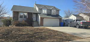 Split level home with brick siding, an attached garage, concrete driveway, and a shingled roof