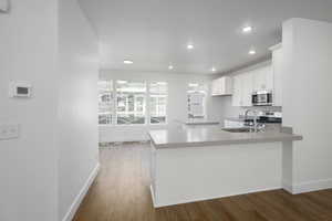 Kitchen with wood finished floors, recessed lighting, a sink, appliances with stainless steel finishes, and white cabinetry