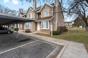 View of front of house with brick siding, a chimney, covered and uncovered parking, and a front yard