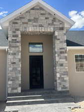 Doorway to property with a shingled roof, stone siding, and stucco siding