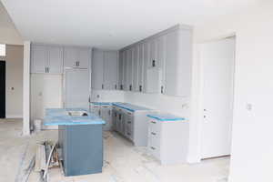 Kitchen featuring gray cabinets, a kitchen island with sink, and fridge