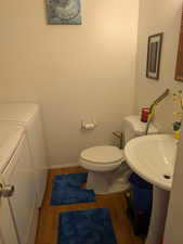 Bathroom with baseboards, wood finished floors, washer and dryer, and toilet