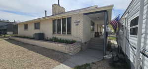 View of side of home with a porch, a chimney, brick siding, and central air condition unit