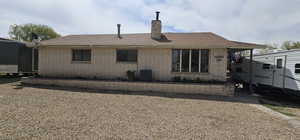 Back of property with central AC, roof with shingles, brick siding, and a chimney