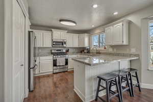 Kitchen featuring a kitchen bar, appliances with stainless steel finishes, a peninsula, white cabinets, and a sink