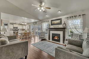 Living area featuring vaulted ceiling, ceiling fan with notable chandelier, a tile fireplace, and wood finished floors