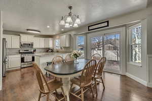 Dining space with a notable chandelier, dark wood-style floors, baseboards, and a textured ceiling