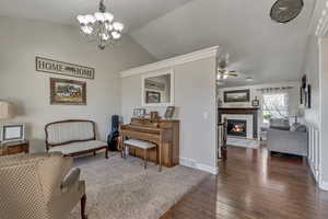 Living area featuring dark wood-style floors, visible vents, a fireplace, vaulted ceiling, and ceiling fan with notable chandelier