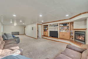 Living area featuring recessed lighting, baseboards, a warm lit fireplace, and light carpet