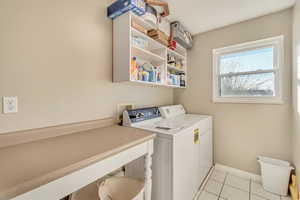 Laundry room featuring baseboards, light tile patterned flooring, laundry area, and washing machine and clothes dryer