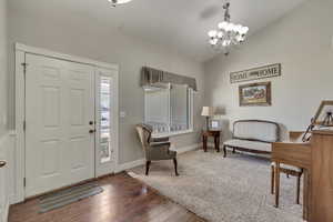 Foyer featuring an inviting chandelier, baseboards, lofted ceiling, and wood finished floors