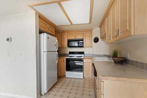 Kitchen featuring black microwave, light floors, electric stove, freestanding refrigerator, and a sink