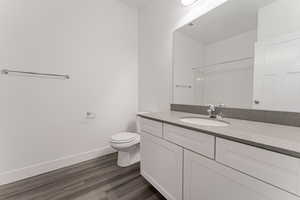 Bathroom featuring vanity, wood finished floors, baseboards, walk in shower, and toilet
