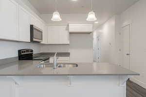 Kitchen featuring light stone countertops, appliances with stainless steel finishes, a peninsula, white cabinetry, and a sink
