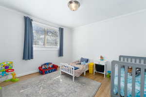 Bedroom featuring a nursery area, wood finished floors, and crown molding