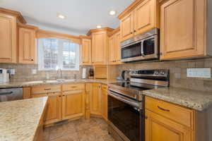 Kitchen with a sink, light stone counters, stainless steel appliances, light tile patterned floors, and decorative backsplash