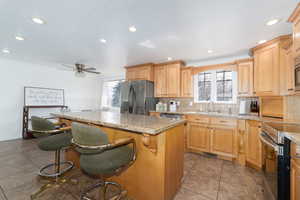 Kitchen featuring tasteful backsplash, a kitchen island, stainless steel appliances, a ceiling fan, and a sink