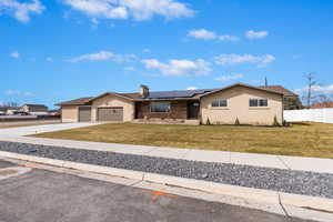 Single story home featuring fence, a front yard, roof mounted solar panels, driveway, and an attached garage