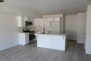 Kitchen featuring light wood-type flooring, a kitchen island with sink, a sink, white cabinetry, and appliances with stainless steel finishes