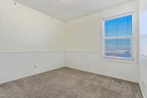 Carpeted empty room featuring window and a wainscoted wall