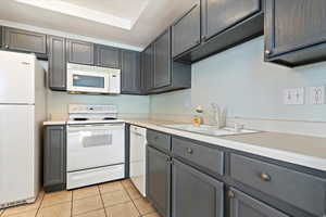 Kitchen featuring gray cabinetry, a sink, white appliances, light countertops, and light tile patterned floors