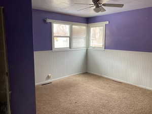 Empty room featuring a wainscoted wall, a textured ceiling, visible vents, and ceiling fan