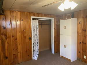 Unfurnished bedroom with a closet, wooden walls, ceiling fan, and carpet flooring