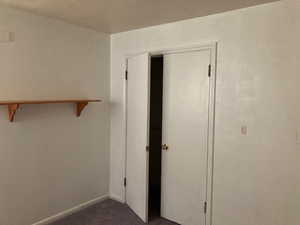 Unfurnished bedroom featuring a closet, dark carpet, a textured ceiling, and baseboards