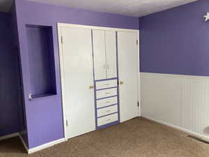 Unfurnished bedroom featuring visible vents, a closet, wainscoting, and carpet flooring