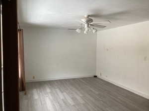 Empty room featuring a textured ceiling, baseboards, a ceiling fan, and wood finished floors