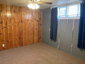 Carpeted spare room with wooden walls and ceiling fan