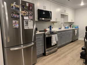 ADU Kitchen with gray cabinets, stainless steel appliances, light wood-type flooring, and light countertops