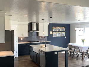 Kitchen with dark wood-type flooring, wall chimney range hood, light countertops, stainless steel appliances, and a sink