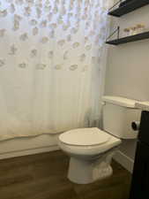 Bathroom with shower / bath combo with shower curtain, toilet, wood finished floors, baseboards, and vanity