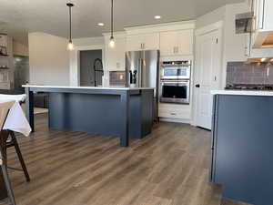 Kitchen with a center island with sink, dark wood-style flooring, stainless steel appliances, light countertops, and white cabinetry
