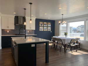 Kitchen with dark wood finished floors, decorative backsplash, light countertops, and wall chimney range hood
