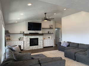 Living room with a ceiling fan, vaulted ceiling, wood finished floors, and a fireplace