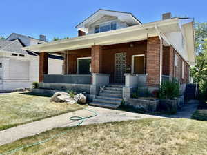 View of front of property with covered porch, brick siding, and a front lawn