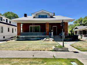 Bungalow-style home featuring a porch, brick siding, a chimney, and a front yard