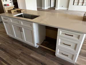 Kitchen featuring dark wood-type flooring, white cabinetry, light stone countertops, and a sink