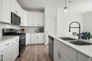 Kitchen with decorative light fixtures, stainless steel appliances, light wood-style floors, white cabinetry, and a sink