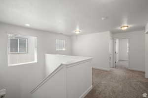 Corridor with baseboards, light colored carpet, and a textured ceiling