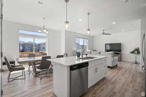 Kitchen with a sink, light countertops, stainless steel dishwasher, light wood-style floors, and a kitchen island with sink