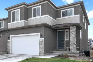 View of front facade with board and batten siding, central air condition unit, an attached garage, and stone siding