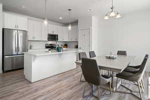 Kitchen with light countertops, white cabinets, appliances with stainless steel finishes, a kitchen bar, and light wood-type flooring