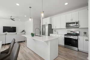 Kitchen with open floor plan, appliances with stainless steel finishes, light wood-style floors, a ceiling fan, and a sink