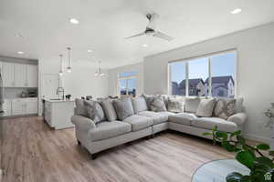 Living room featuring ceiling fan with notable chandelier, recessed lighting, baseboards, and light wood finished floors